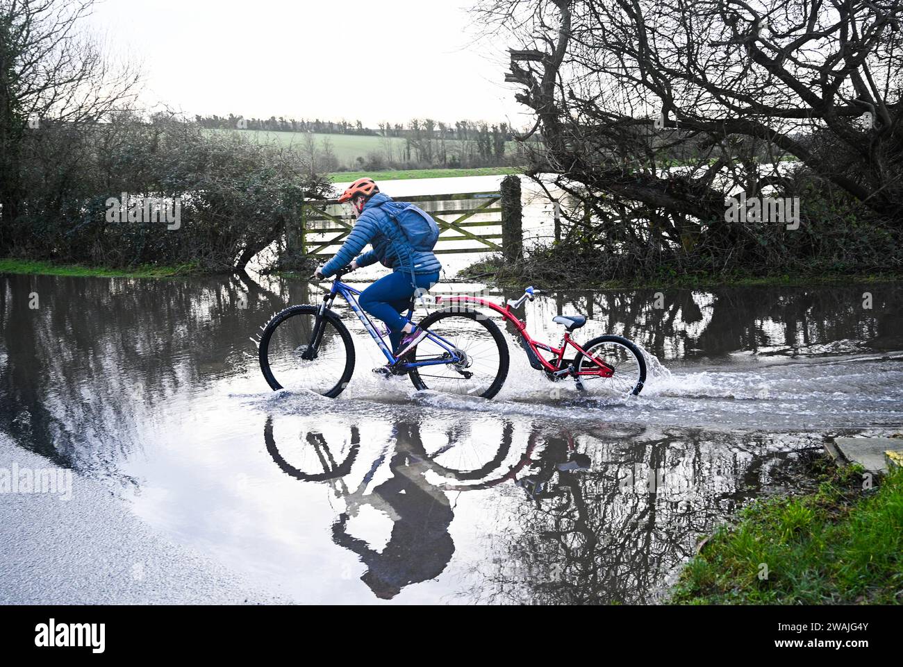 Alfriston, Sussex UK 5. Januar 2024 - Ein Radfahrer reitet durch das Hochwasser auf den Straßen um das Dorf Alfriston in East Sussex nach einer weiteren Nacht mit starkem Regen mit über 300 Überschwemmungen und Wetterwarnungen im ganzen Land: Credit Simon Dack / Alamy Live News Stockfoto