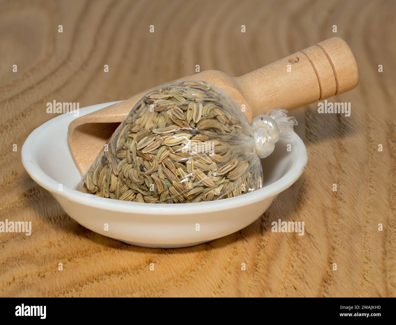 Kleine Frischhaltefolie aus rohen getrockneten Fenchelsamen in einer weißen Keramikschale und Bambuslöffel auf einer hölzernen Küchenplatte Stockfoto