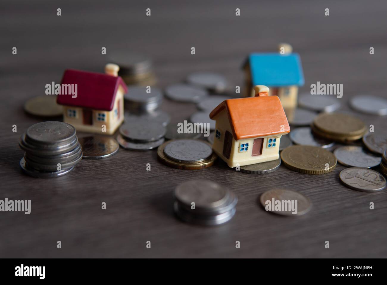 Nahaufnahme eines Spielzeughauses, umgeben von Münzen. Kopierbereich für Text. Hauseigentum-Konzept. Stockfoto