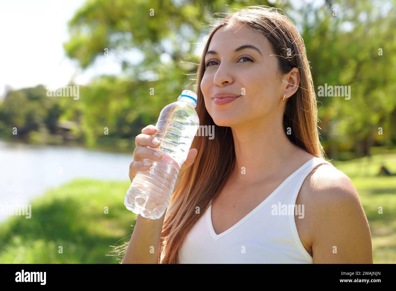 Attraktive Fitness-Frau, die wegschaut und eine Flasche Wasser hält, um im Stadtpark zu trinken Stockfoto