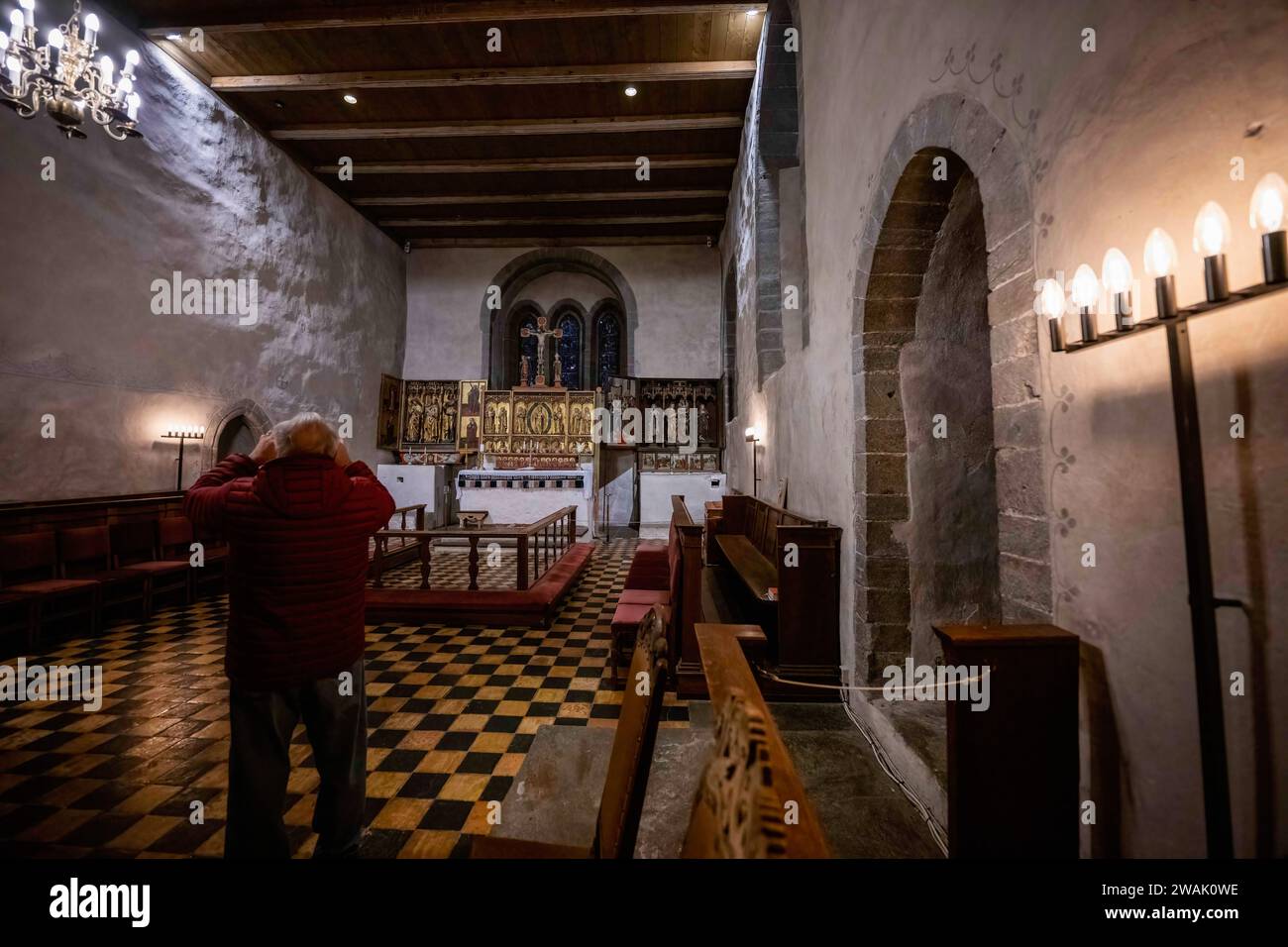 Ein Tourist spaziert um den Hauptaltar der mittelalterlichen Kirche von Tondenes, die um 1435 erbaut wurde und für ihre historische Architektur und kulturelle Bedeutung bekannt ist. Trondenes ist eine Stadt im Norden Norwegens in der Region Troms og Finnmark. Umgeben von einer atemberaubenden arktischen Landschaft mit Fjorden und Bergen hat die Region eine reiche Fischertradition. Trondenes zieht Besucher an, die sich für Geschichte und natürliche Schönheit interessieren. Stockfoto