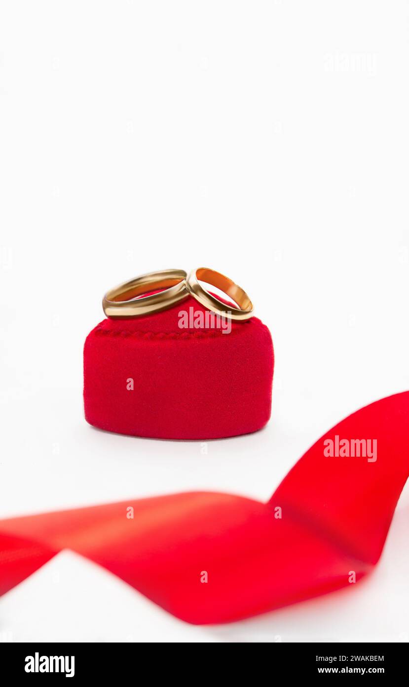 Goldene Eheringe auf rotem Samtgeschenkkasten Herz mit Band auf weißem Hintergrund. Ehe, Vorschlag, Valentinstag. Vertikal. Kopierbereich Stockfoto
