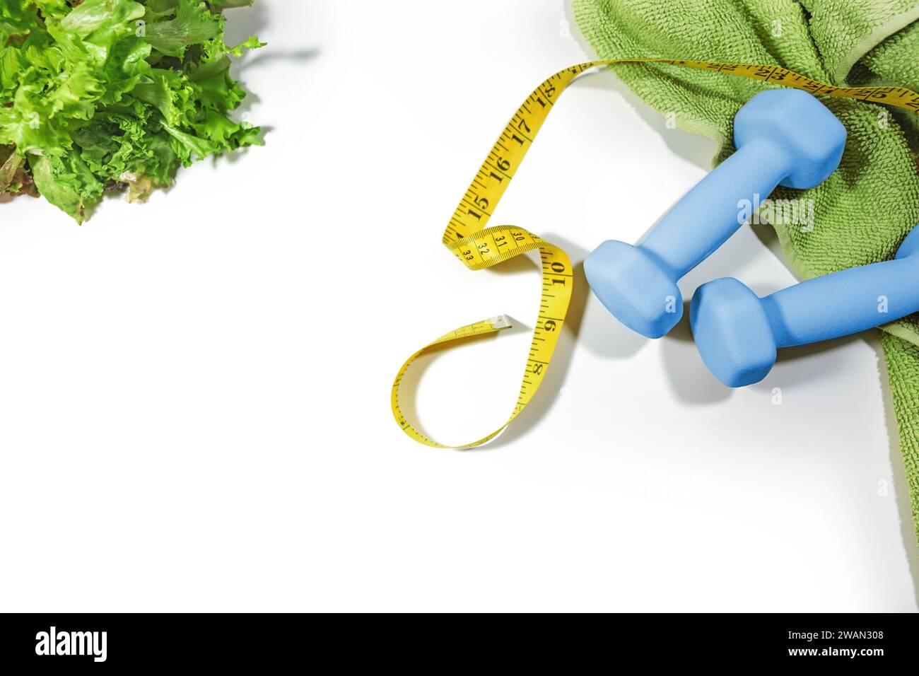 Abnehmen mit einer gesunden Ernährung und Sport für Fitness, symbolisiert durch Kurzhanteln, grünes Handtuch, gelbes Maßband und Salat, Blick von oben auf A Stockfoto