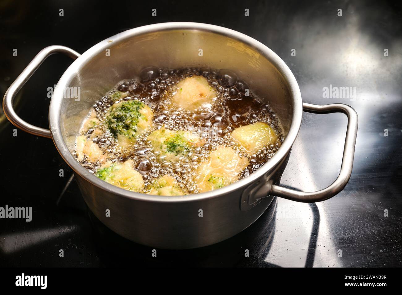 Blumenkohl und Brokkoli werden in einem Topf mit heißem kochendem Öl auf einem schwarzen Herd frittiert und kochen einen leckeren veganen Snack mit Gemüse, Stockfoto