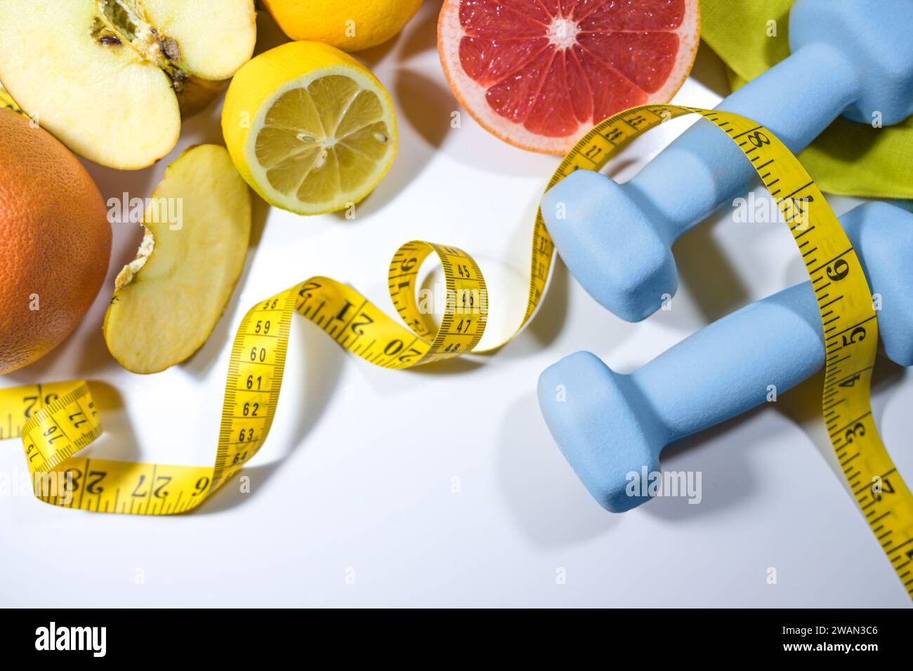 Gesunder Lebensstil, Fitness und Schlankheitsgefühl symbolisiert durch frisches Obst, Maßband und Kurzhanteln für Sport auf einem hellgrauen Hintergrund, Hochwinkelansicht Stockfoto