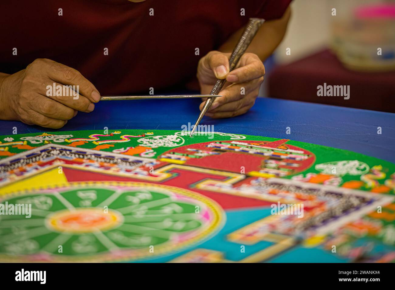 Selektives Nahaufnahme eines tibetischen buddhistischen Mönchs, während er an der Erstellung eines heiligen Mandalas oder Sandgemäldes arbeitet. Stockfoto