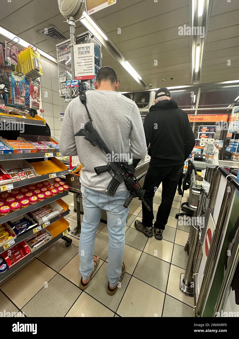 Ein israelischer Mann mit einem Sturmgewehr auf dem Rücken steht in einer Schlange an einer Kasse in einem Supermarkt in Jerusalem Israel Stockfoto