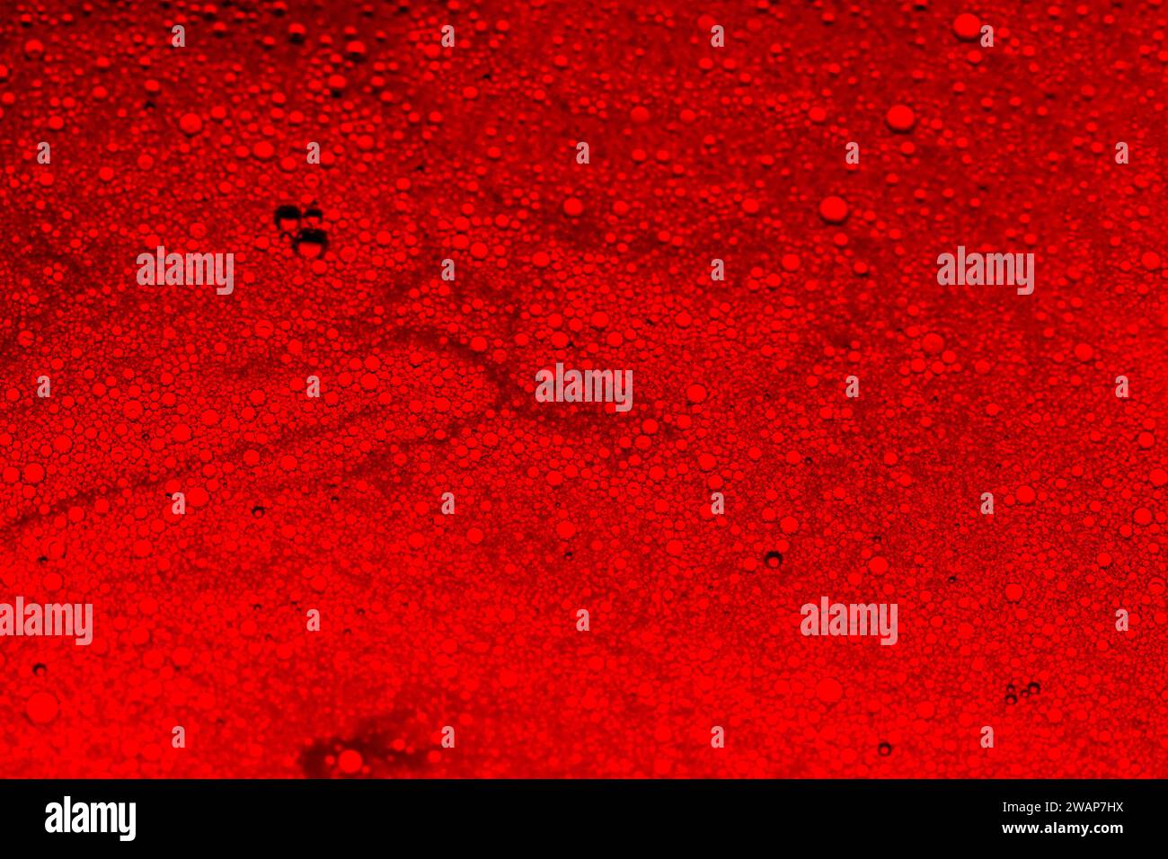 Blasen, die mit Seife und Wasser in Speiseöl mit Hintergrundbeleuchtung durch rotes Foto-Gel gemischt werden Stockfoto