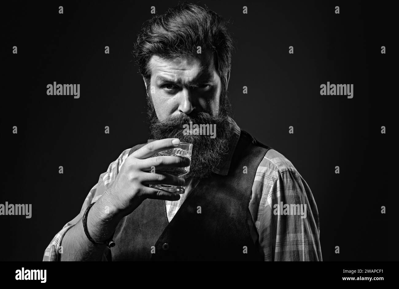 Selbstbewusster, gut gekleideter Mann mit einem Glas Whisky. Mann mit Bart hält Glasschnaps. Der Barkeeper oder Barkeeper serviert Cognac. Stockfoto