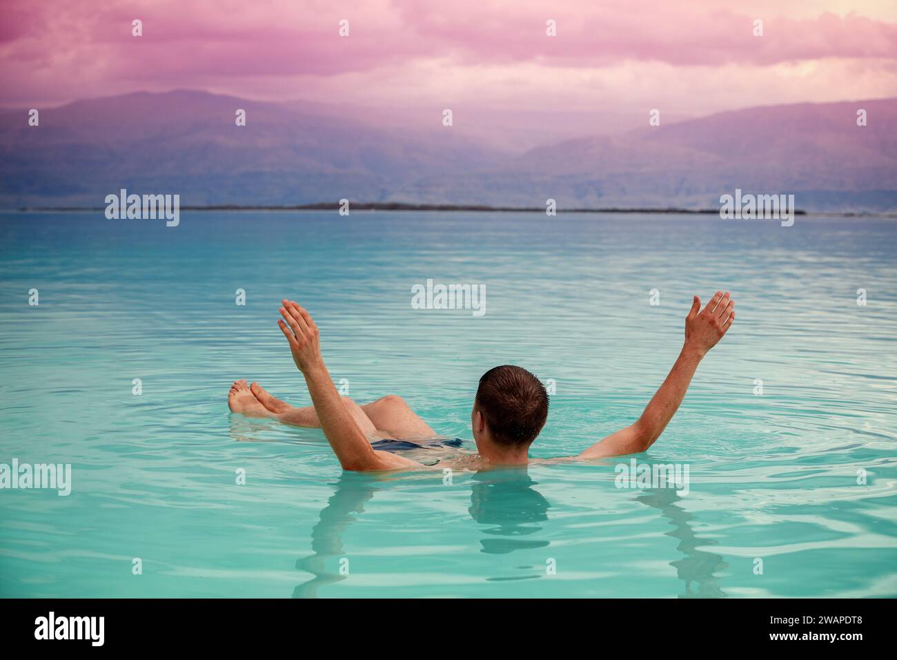 Ein Mann mit Händen in der Luft, der im Toten Meer schwimmt. Kurbehandlungen Stockfoto