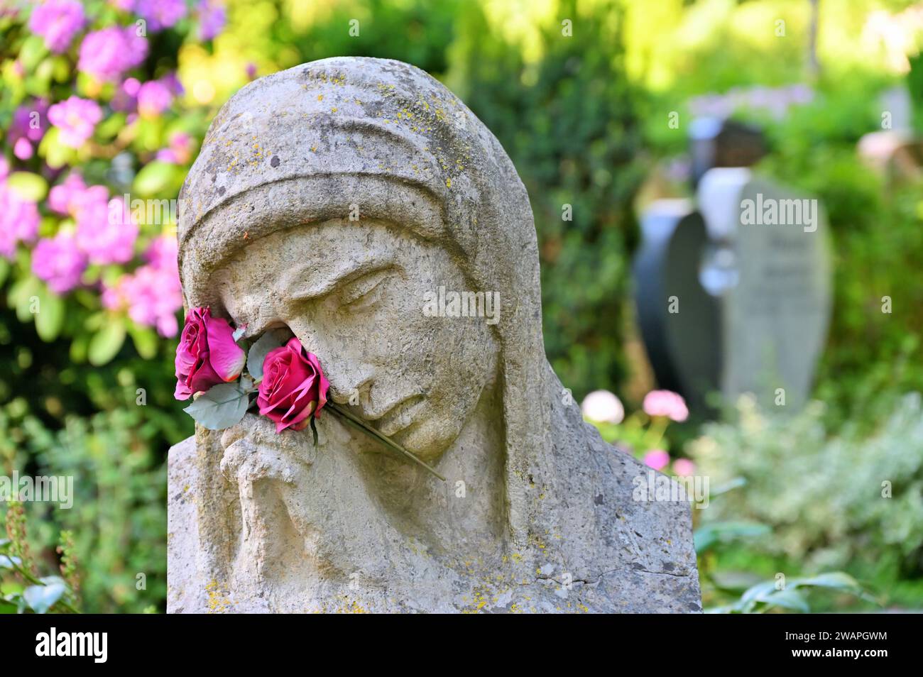 Die Trauerstatue mit betenden Händen und Blumen vor Gräbern Stockfoto