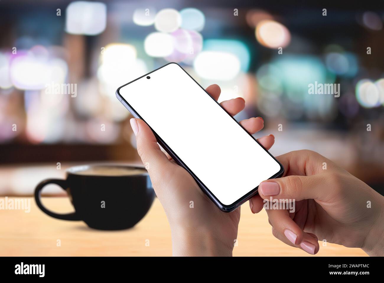 Smartphone-Mockup in den Händen mit Kaffeetasse auf dem Tisch für ein gemütliches Coffee Time-Lesekonzept. Perfekt für die Präsentation digitaler Inhalte im Handumdrehen Stockfoto