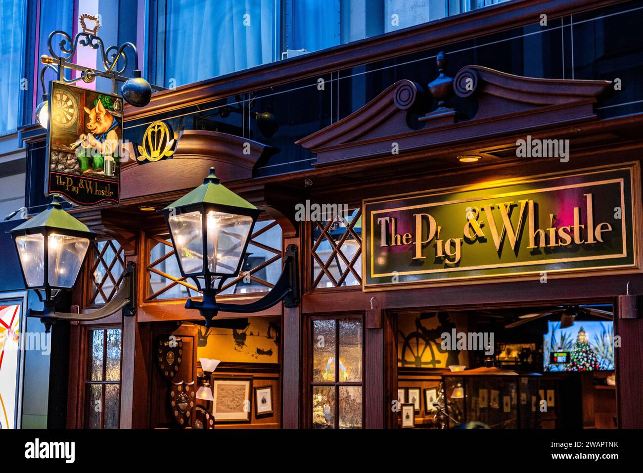 Eine lebhafte Nachtszene, die den traditionellen Pub „Pig and Whistle“ zeigt, beleuchtet von warmgelbem Licht Stockfoto