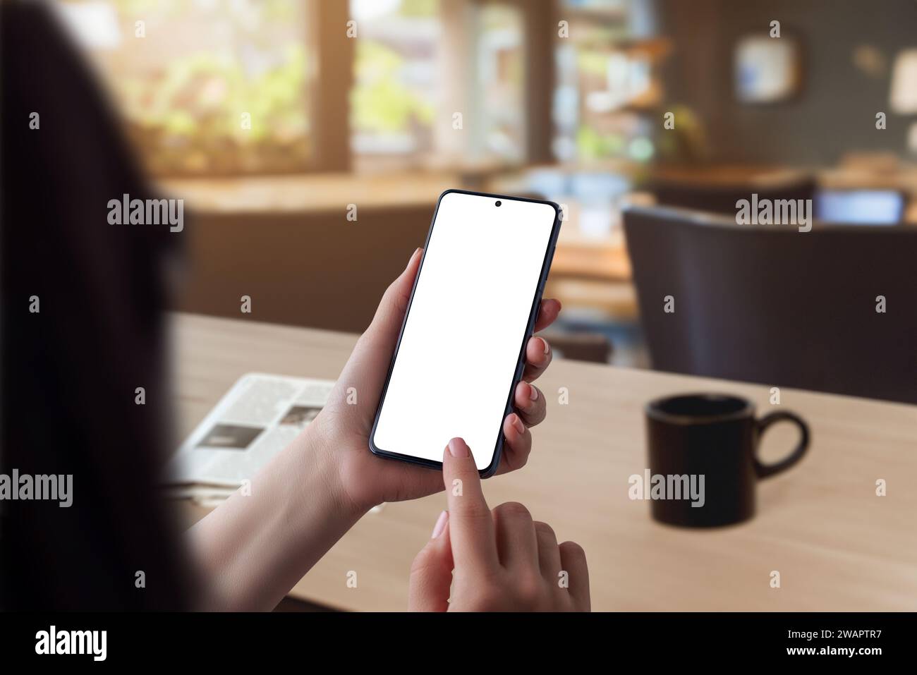 Kaffeeszene am Morgen. Frau mit Smartphone mit isoliertem Bildschirm für App-Präsentation, begleitet von einer Zeitung auf dem Tisch. Perfekt für Showcas Stockfoto