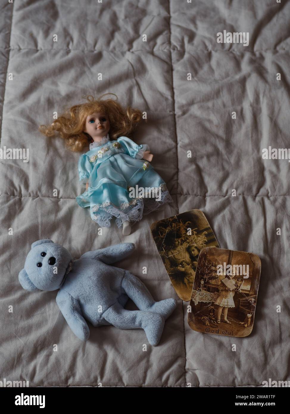 Senkrecht gerade von oben Nahaufnahme eines blauen Teddybären, lockige Retro-Puppe in einem blauen Kleid und zwei Vintage-inspirierte Fotos auf dem Bett. Stockfoto