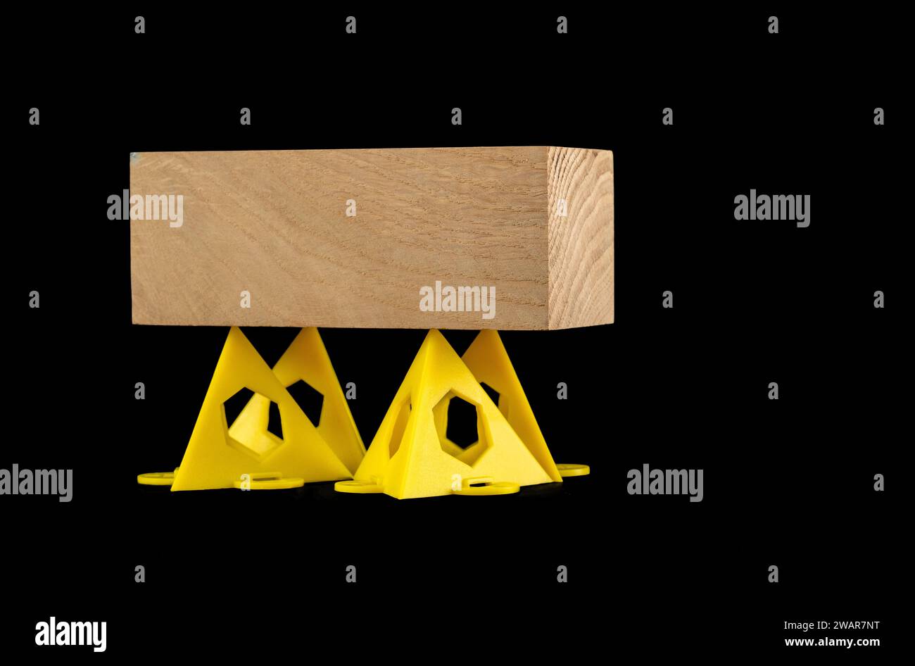 Holzblock, der auf gelben stapelbaren Malern gestützt wird, zeigt Pyramidendreiecke isoliert auf schwarzem Hintergrund Stockfoto