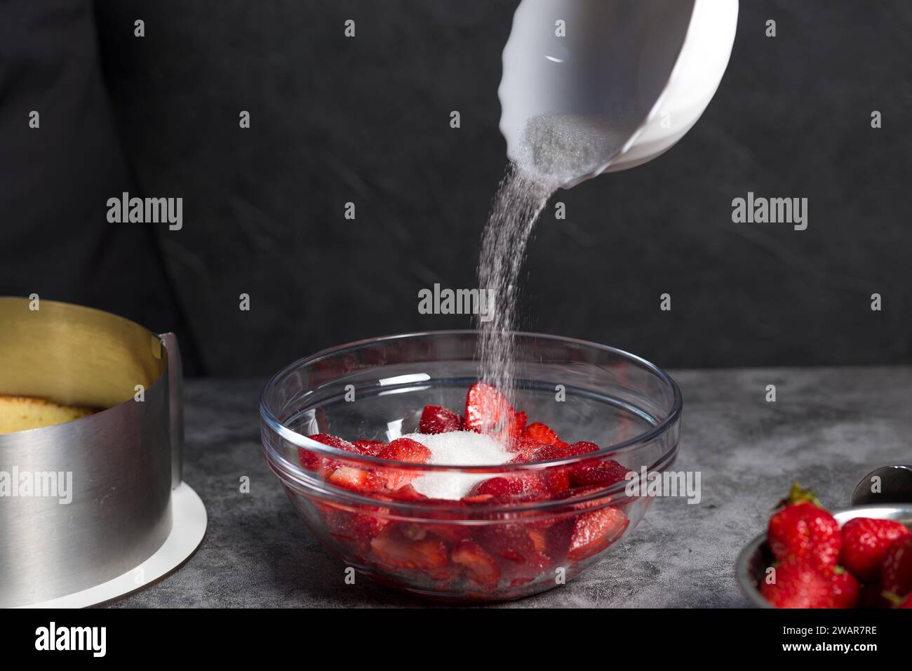 Zucker wird auf dunklem Hintergrund in Erdbeeren gegossen Stockfoto