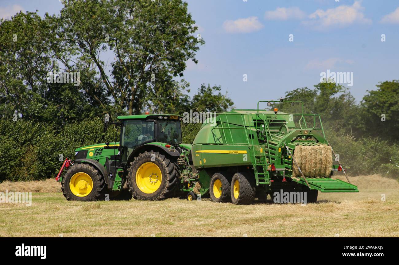 John Deere 6155R-Traktor mit einer L1534-Ballenpresse in der Landschaft von Wiltshire an einem sonnigen Sommertag. Stockfoto
