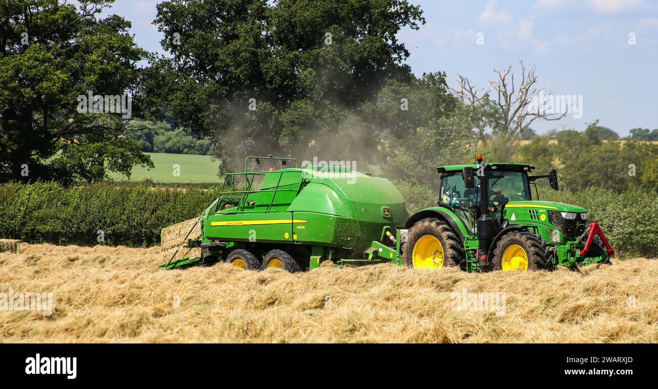 John Deere 6155R-Traktor mit einer L1534-Ballenpresse in der Landschaft von Wiltshire an einem sonnigen Sommertag. Stockfoto