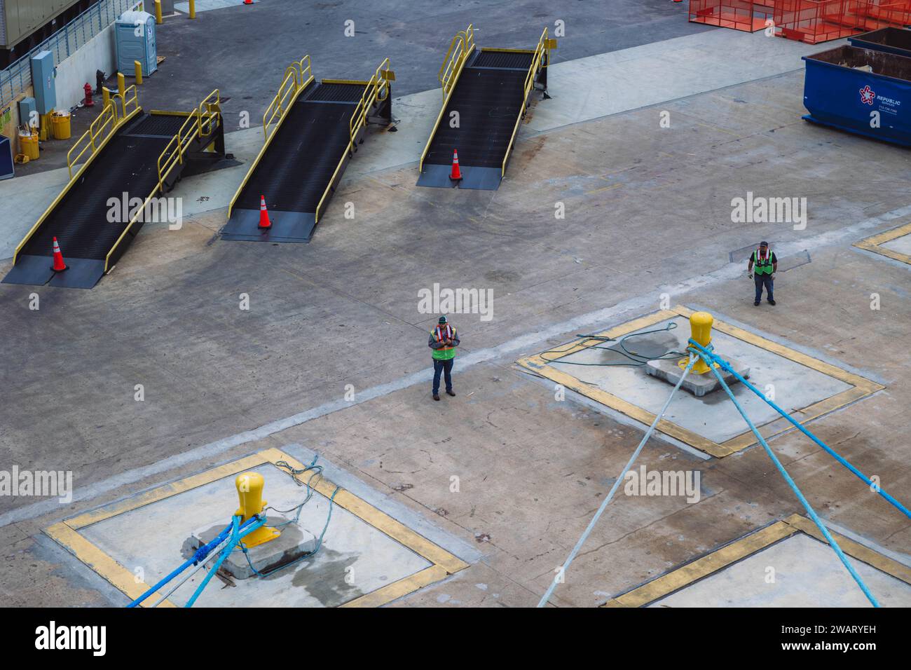 Ein Paar Arbeiter arbeitet hart daran, Rampen für ein Kreuzfahrtschiff in einem stark frequentierten Hafen vorzubereiten Stockfoto
