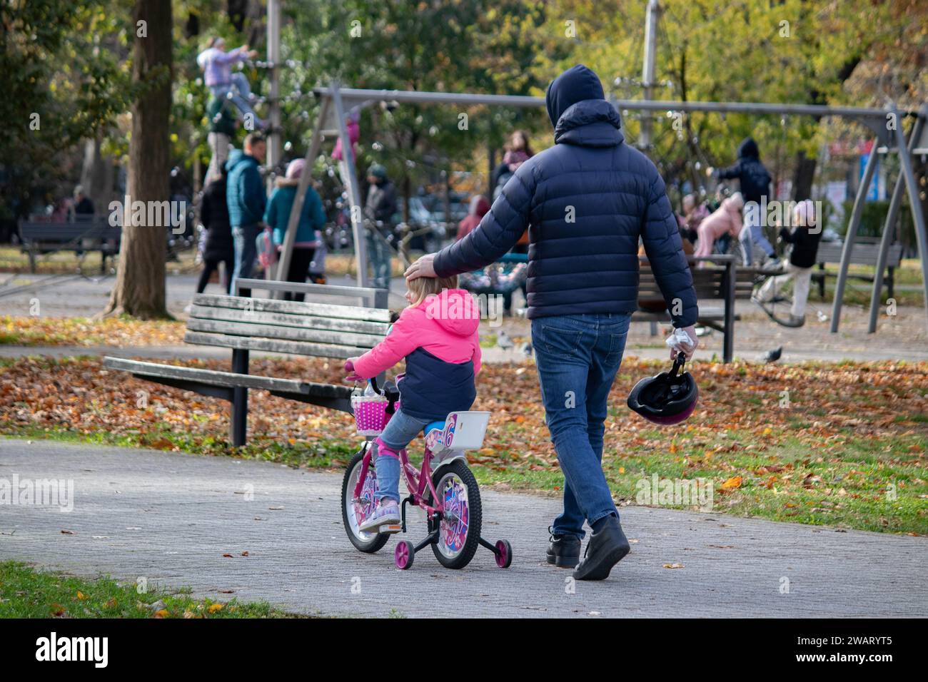 Vater spaziert und Tochter auf dem Fahrrad auf dem Weg zum Spielplatz im öffentlichen Park in Belgrad, Tasmajdan Park, in der Nähe der Marko Kirche Stockfoto