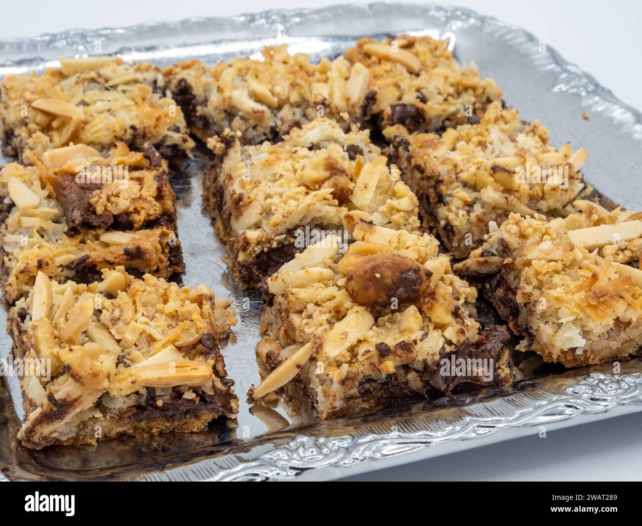 Eine köstliche Auswahl an Brownies mit goldenen Mandelflocken, bereit, im Mund zu schmelzen. Präsentiert auf Metallplatte isoliert auf weißem Hintergrund. Stockfoto