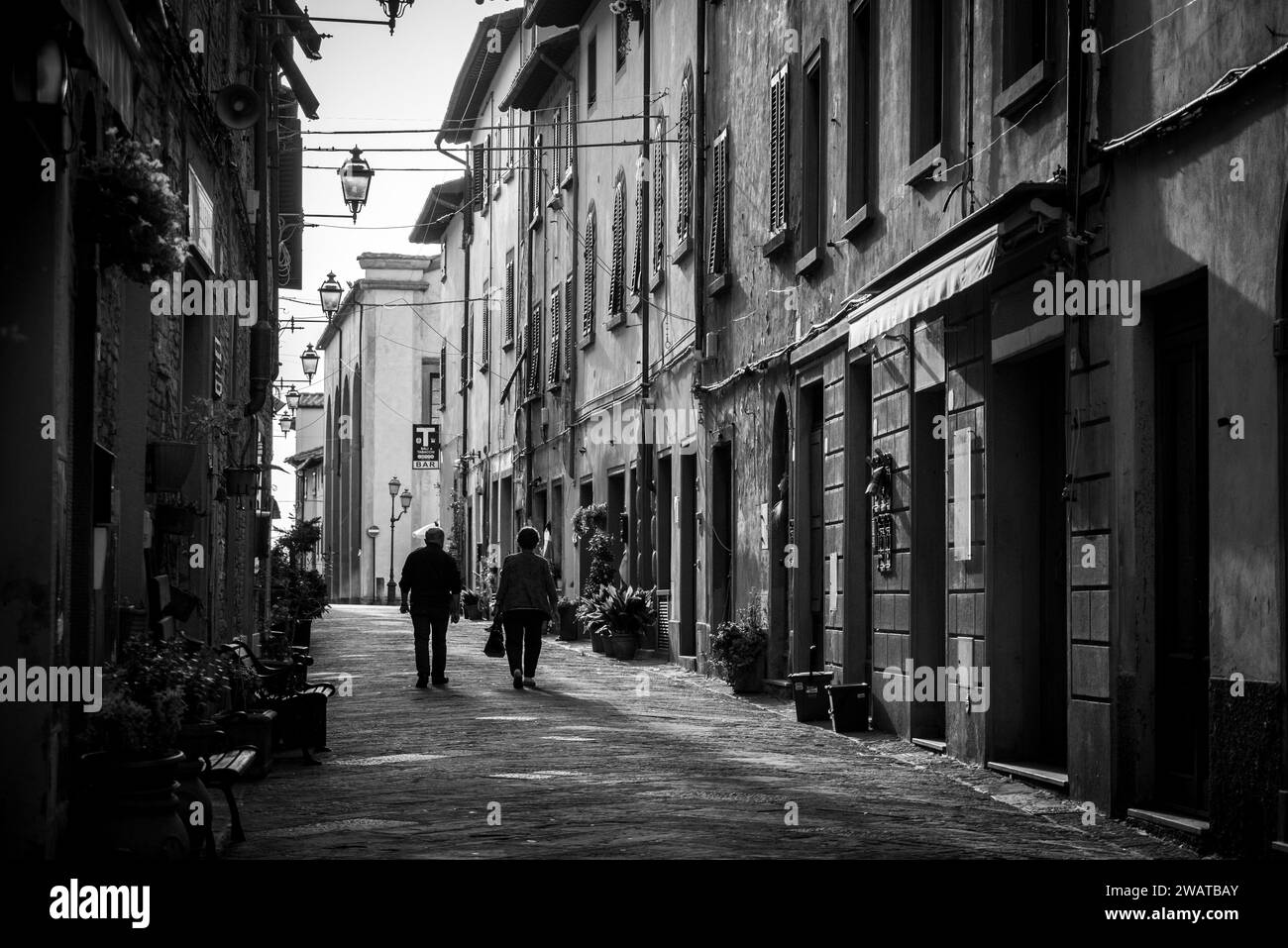 Ein älteres Paar, das am frühen Morgen durch eine leere Gasse von Montaione in der Toskana spaziert, Italien Stockfoto