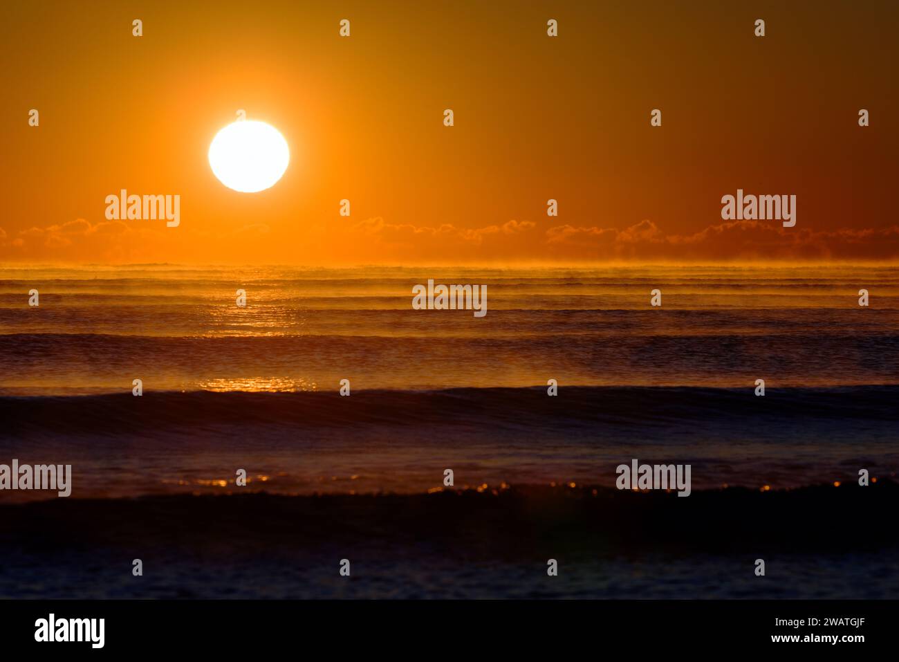 Atlantisches Erwachen: Majestätischer Sonnenaufgang, der ein warmes Orange über die nebligen Wellen des Ozeans wirft Stockfoto