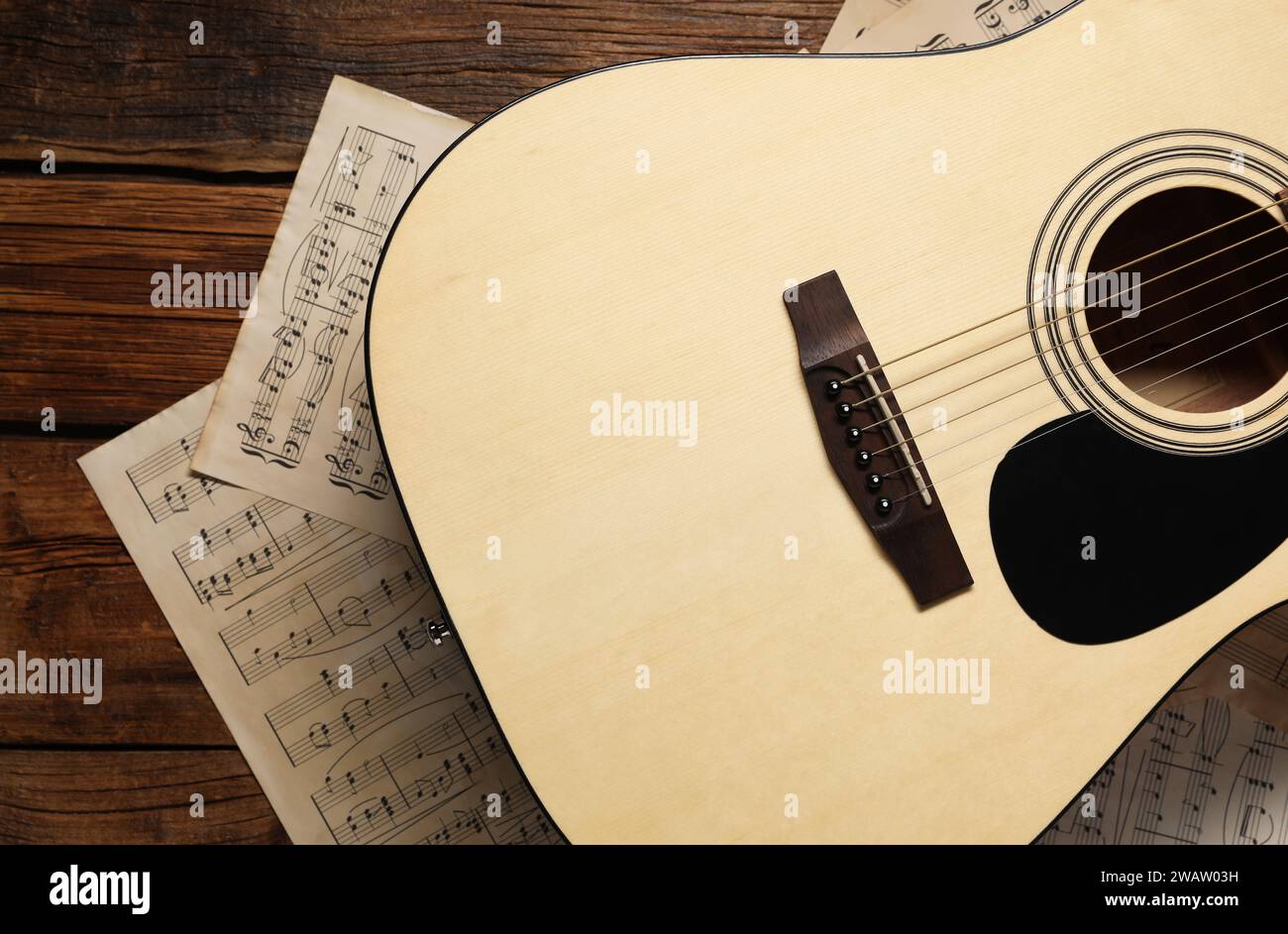 Papierbögen mit Musiknoten und Akustikgitarre auf Holztisch, Blick von oben Stockfoto