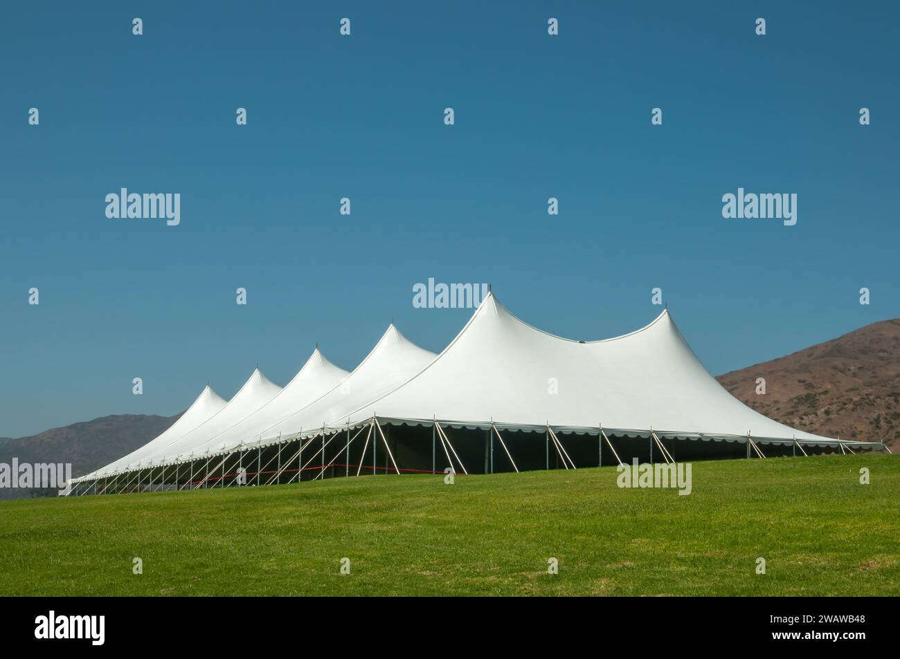 Großes weißes Zelt für Veranstaltungen in einem grünen Feld, mit Bergen im Hintergrund Stockfoto
