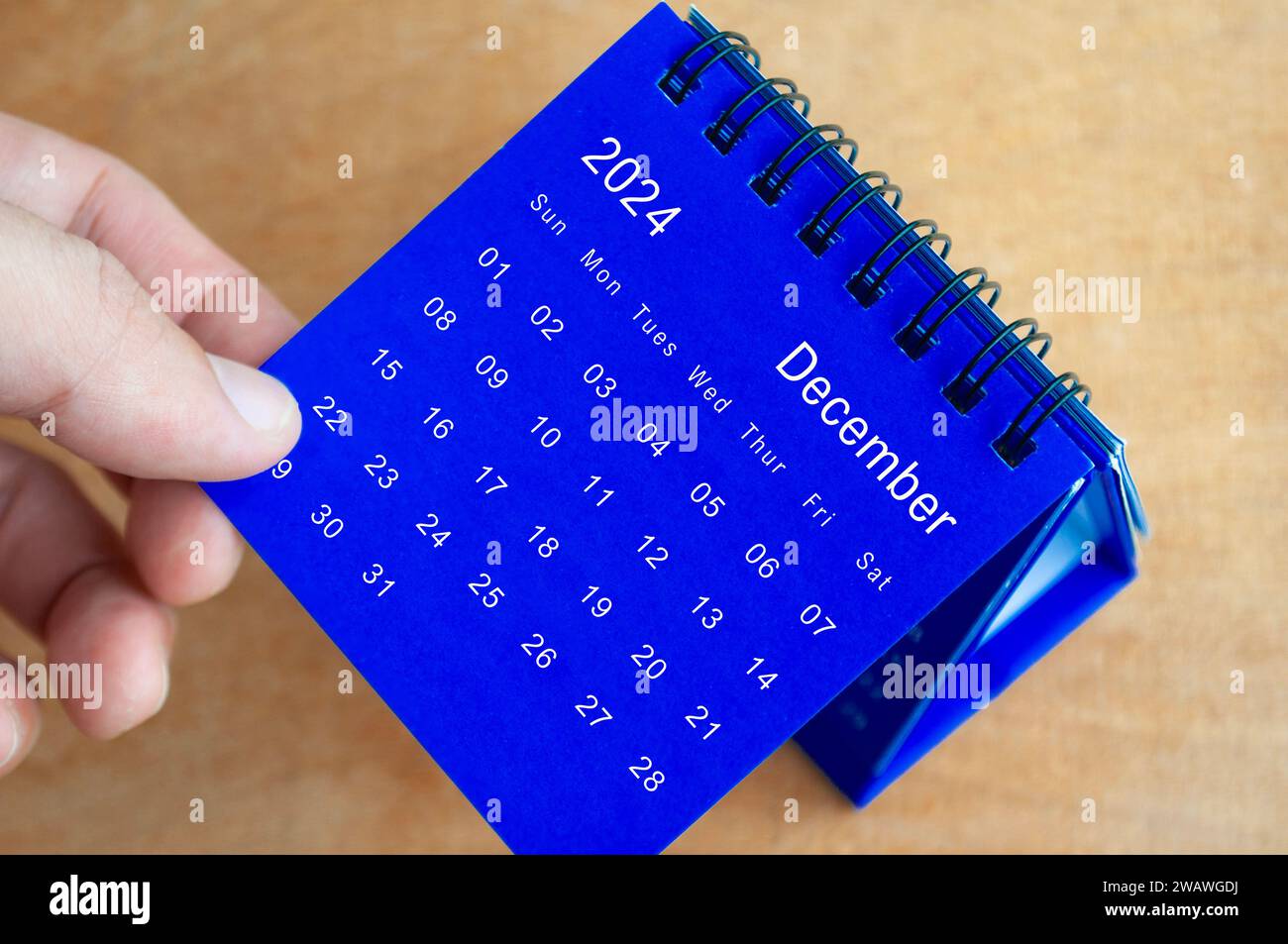 Hand mit Tischkalender Dezember 2024 auf hölzernem Hintergrund. Kalenderkonzept. Stockfoto