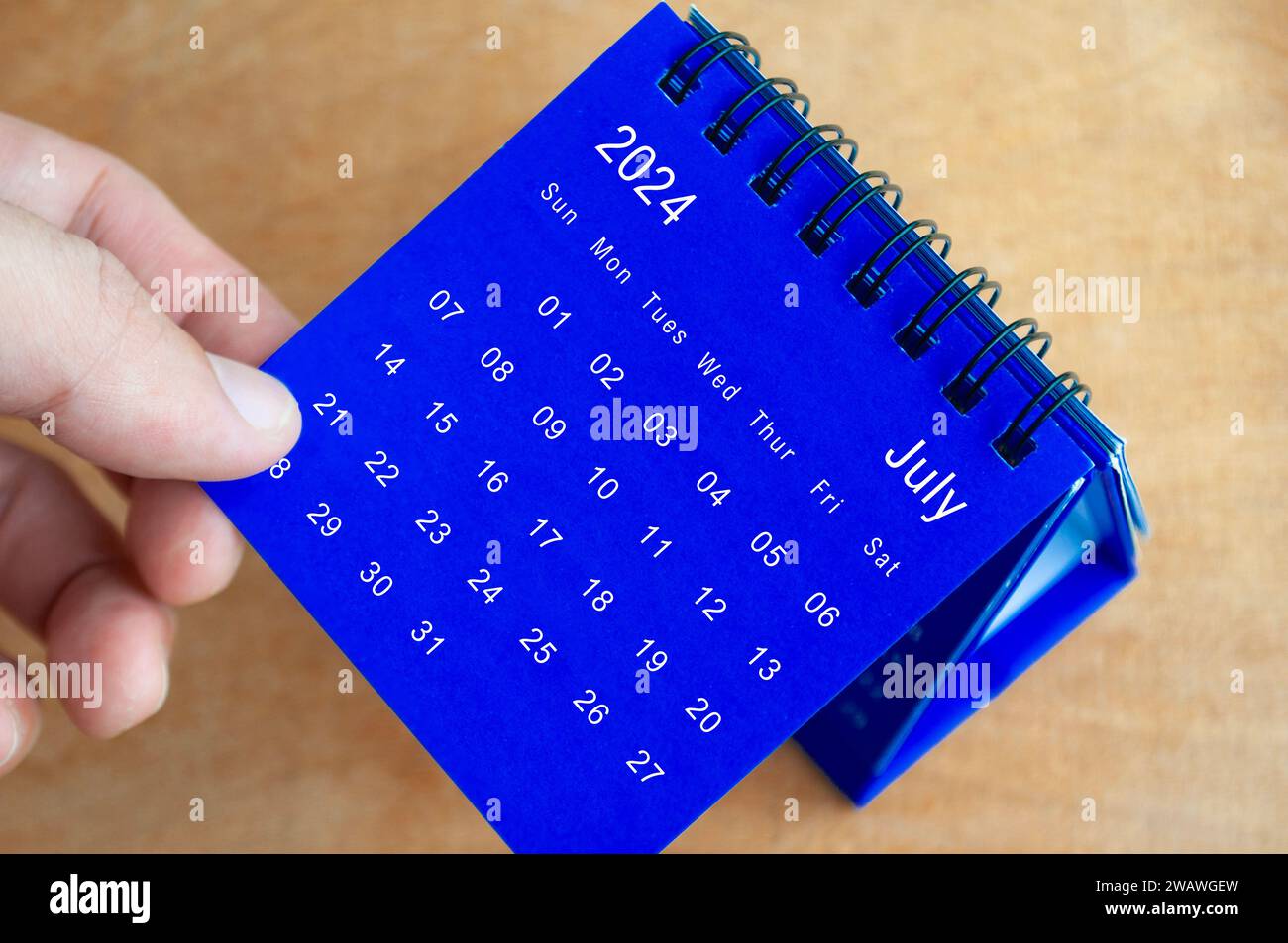 Hand mit Tischkalender Juli 2024 auf hölzernem Hintergrund. Kalenderkonzept. Stockfoto