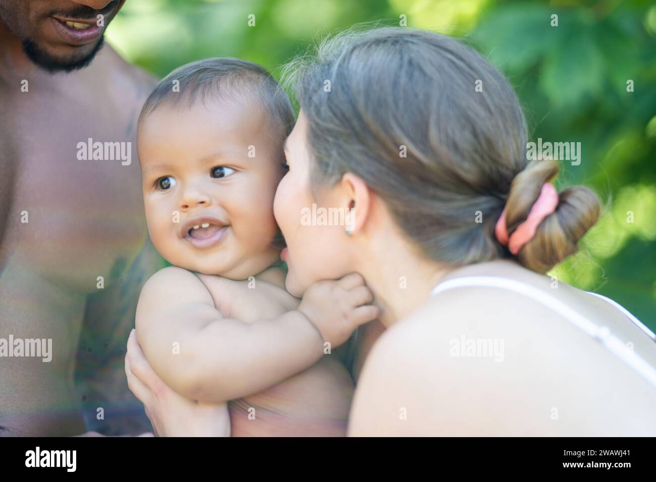 Glückliche multiethnische Eltern und stauntes Baby mit gemischter Rasse. Outdoor-Porträt für gemischte Rassen. Glückliche birassische Familie umarmt Ihr Kind. Wunderschön vielfältig Stockfoto