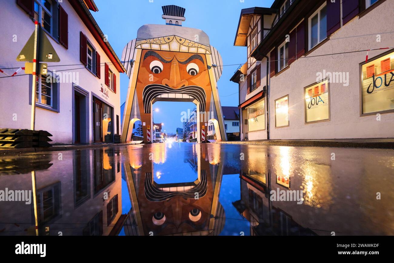 07. Januar 2024, Baden-Württemberg, Riedlingen: Der Goletor steht am Eingang zur Altstadt von Riedlingen und spiegelt sich in einer Regenpfütze wider. Das Tor zeigt den überdimensionalen Kopf der „Gole“, eine der Riedlinger Fasnet-Figuren aus dem Jahr 1890. Das Tor wird nur zu besonderen Anlässen in der Donaustadt errichtet. Grund dafür ist die Karnevalssitzung der Vereinigung Schwäbisch Alemannischer Narrenzünfte (VSAN) am 04.02.2024. Wer in die Riedlinger Innenstadt kommt, sieht nun die rollenden Augen der mächtigen „Gole“ aus der Ferne und kann nur noch die historische Altstadt betreten Stockfoto