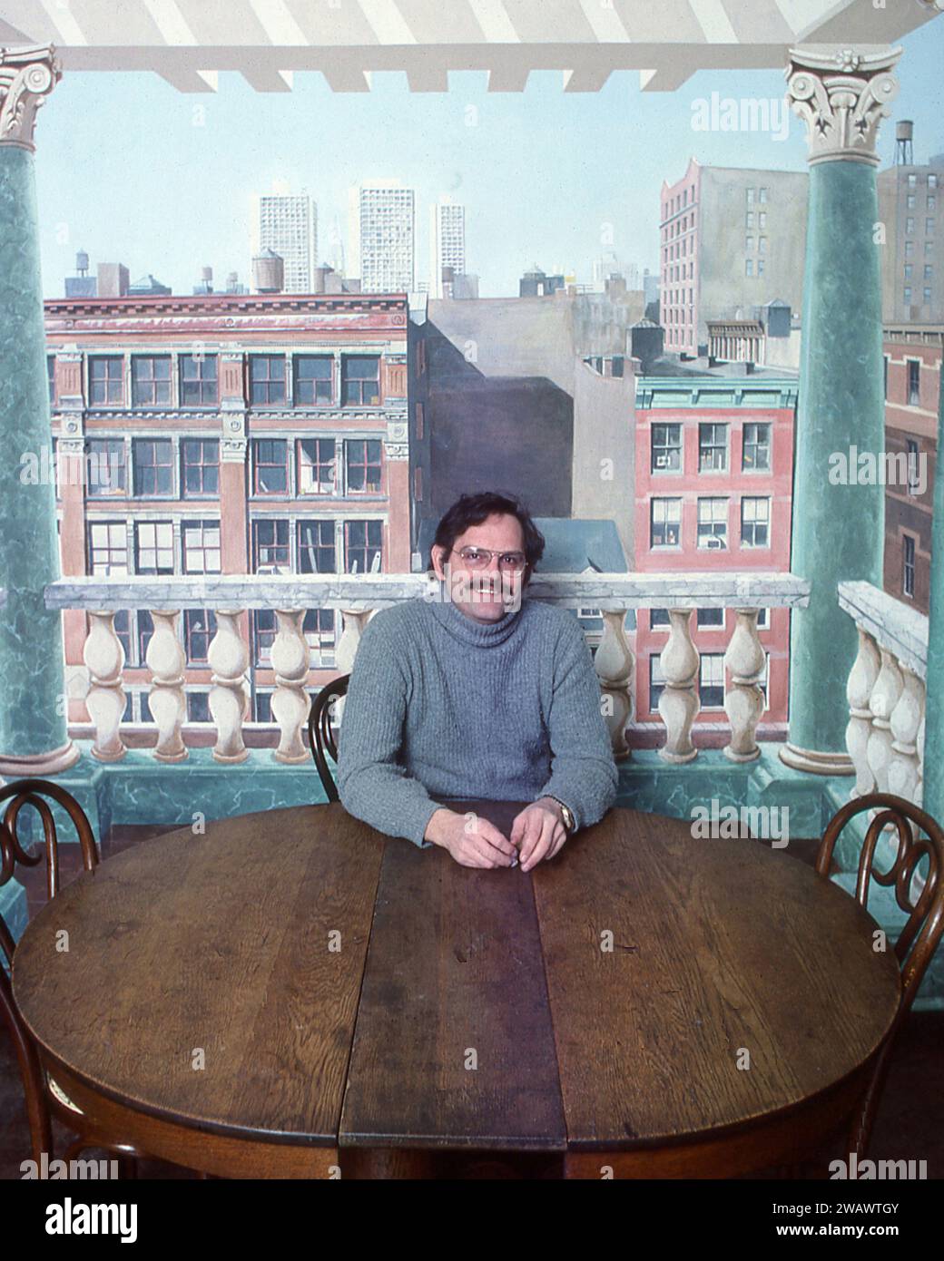 Der Trompe-L'Oiel-Künstler Richard Haas sitzt vor einer seiner Werke. 1977 in seinem Greenwich Village Loft in Soho, New York City. Er malte eine Terrasse mit Aussicht, genau die Aussicht, die er hätte, wenn er eine richtige Terrasse hätte. Stockfoto