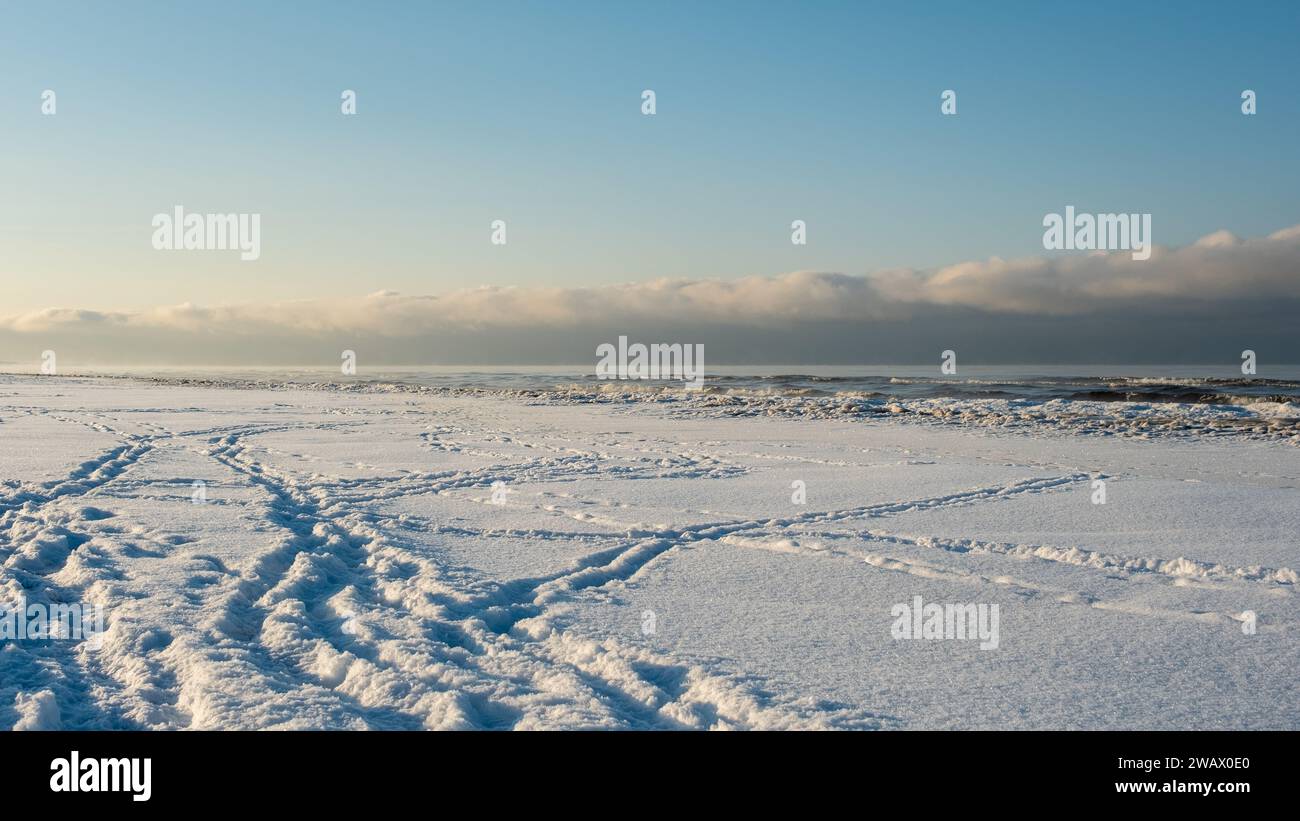 Die Magie der Golden Hour schlängelt sich durch die verschneite Küste, ein flüchtiger Moment von heiterer Schönheit. Stockfoto