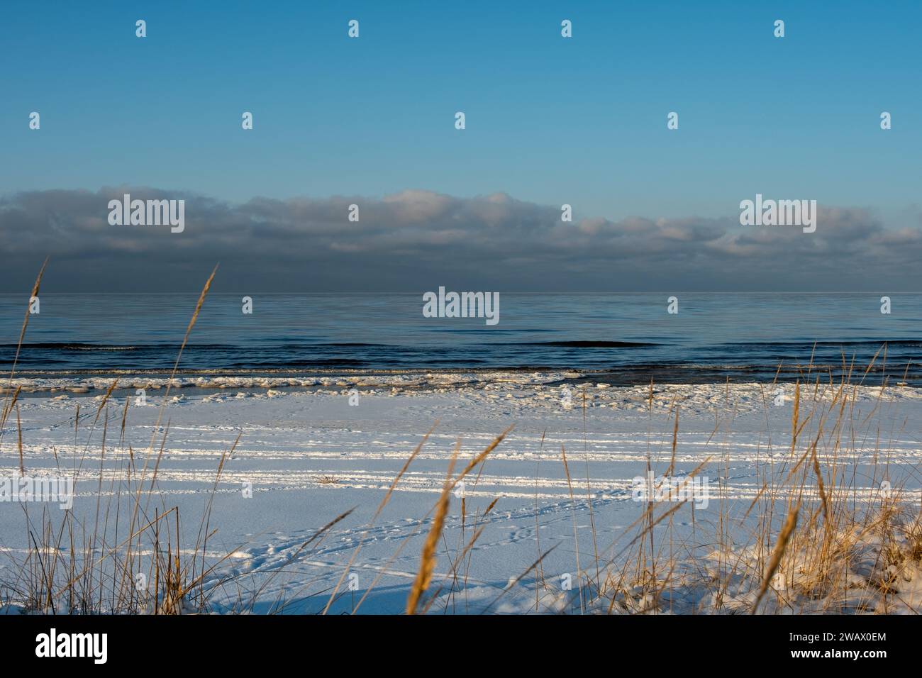 Goldene Farbtöne küssen die verschneite Küste, eine ruhige Umarmung zwischen Winter und Meer. Stockfoto