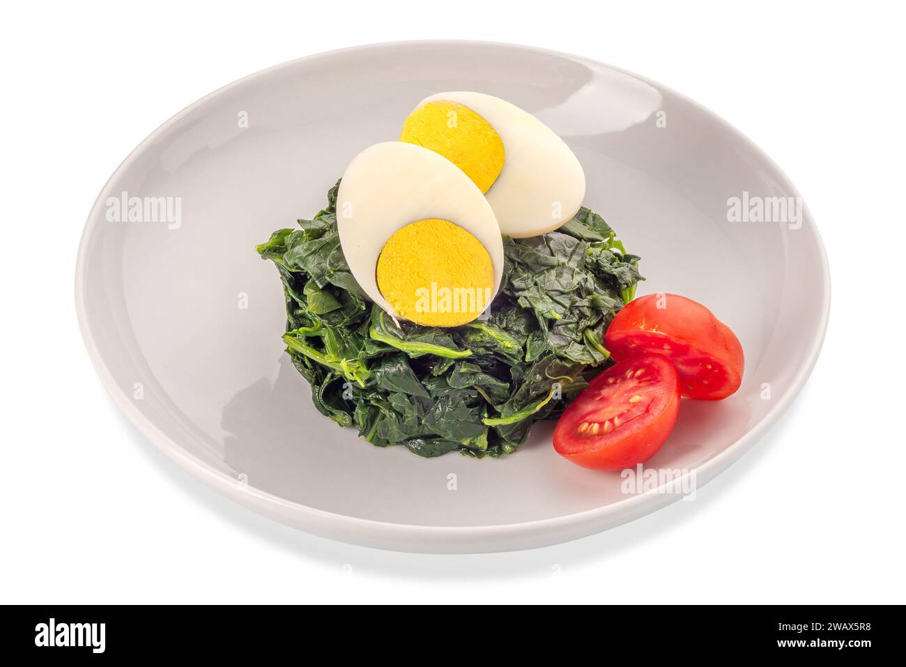 Spinat gekocht mit geschnittenem hartgekochtem Ei und Kirschtomate in weißer Schale isoliert auf weiß mit Schnittpfad enthalten Stockfoto