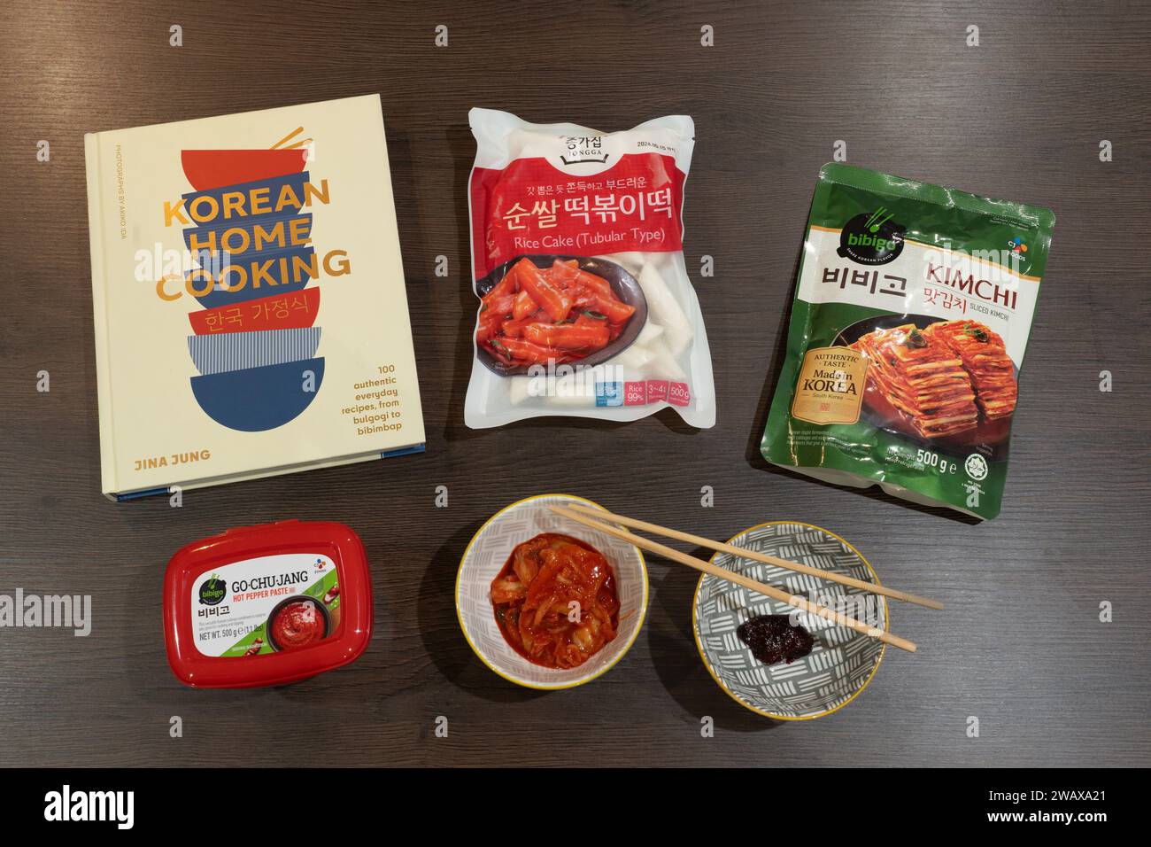 Koreanische Hausmannskost mit einem koreanischen Kochbuch und koreanischen Zutaten: Kimchi, Go Chu Jang heiße Pfefferpaste und röhrenförmige Reiskuchen mit Essstäbchen. UK Stockfoto