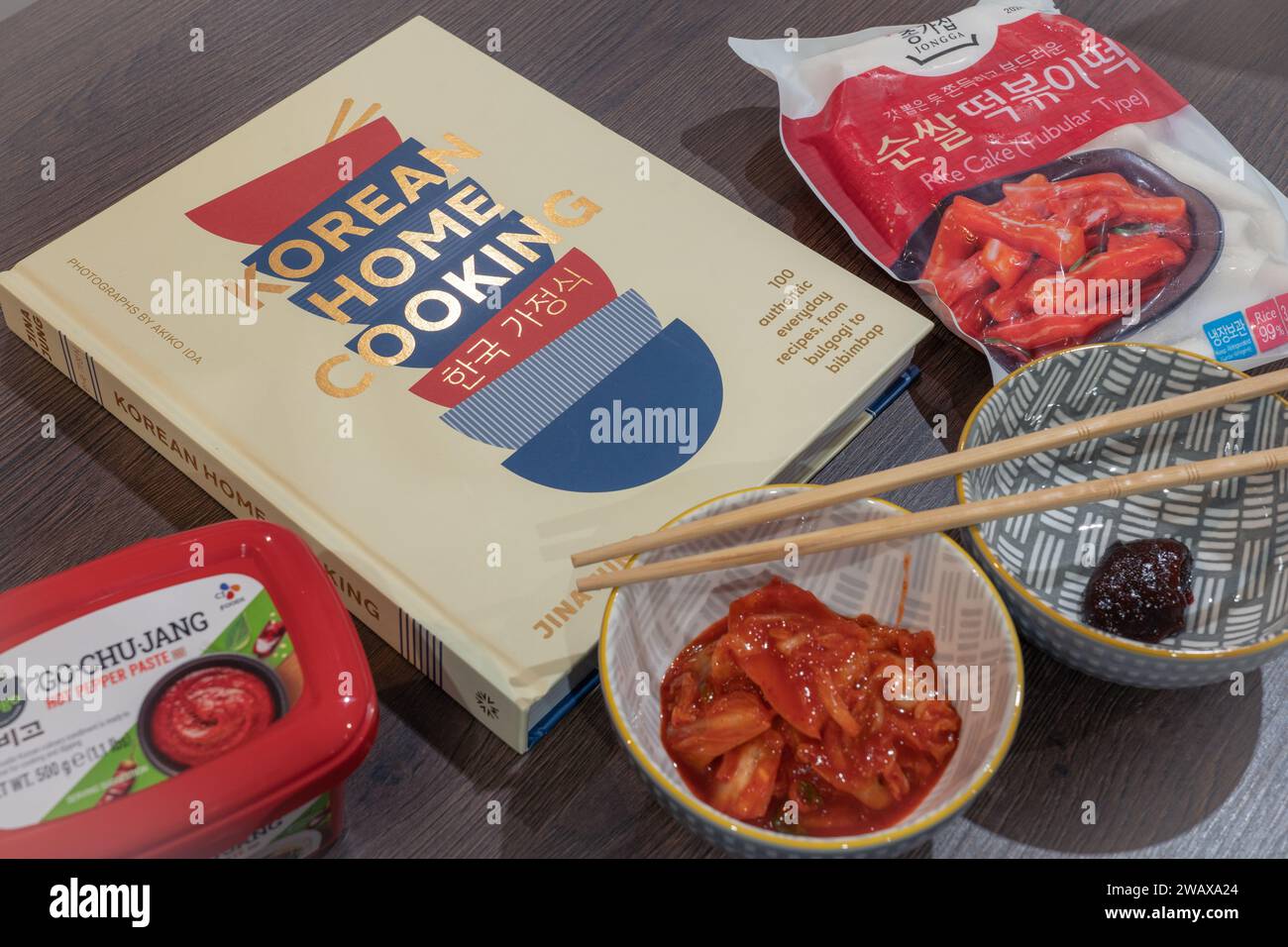 Koreanische Hausmannskost mit einem koreanischen Kochbuch und koreanischen Zutaten: Kimchi, Go Chu Jang heiße Pfefferpaste und röhrenförmige Reiskuchen mit Essstäbchen. UK Stockfoto