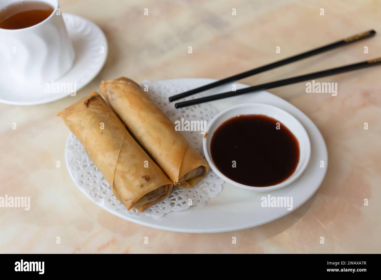 Traditionelles chinesisches Entenfrühlingsbrötchen mit hoi-sin-Sauce und Oolong-Tee mit schwarzen Hackstäbchen in einem chinesischen Restaurant in Großbritannien Stockfoto