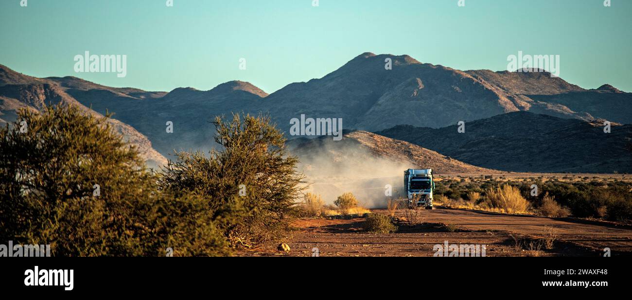 Großer Lkw, der eine Staubwolke von einer Feldstraße in den Bergen Namibias im frühen Morgenlicht hochwirft. Stockfoto