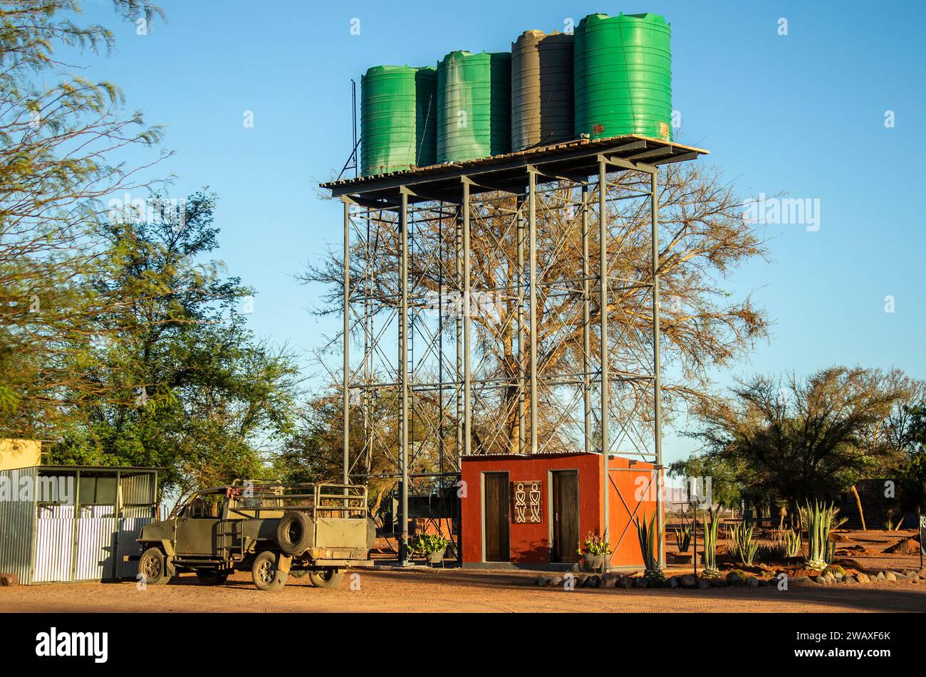 Hausgemachte Gerüste Wasserturm, Toiletten mit humorvollen Schildern und eine alte, khakifarbene Abholung auf einer Farm in der Wüste Namibias. Stockfoto