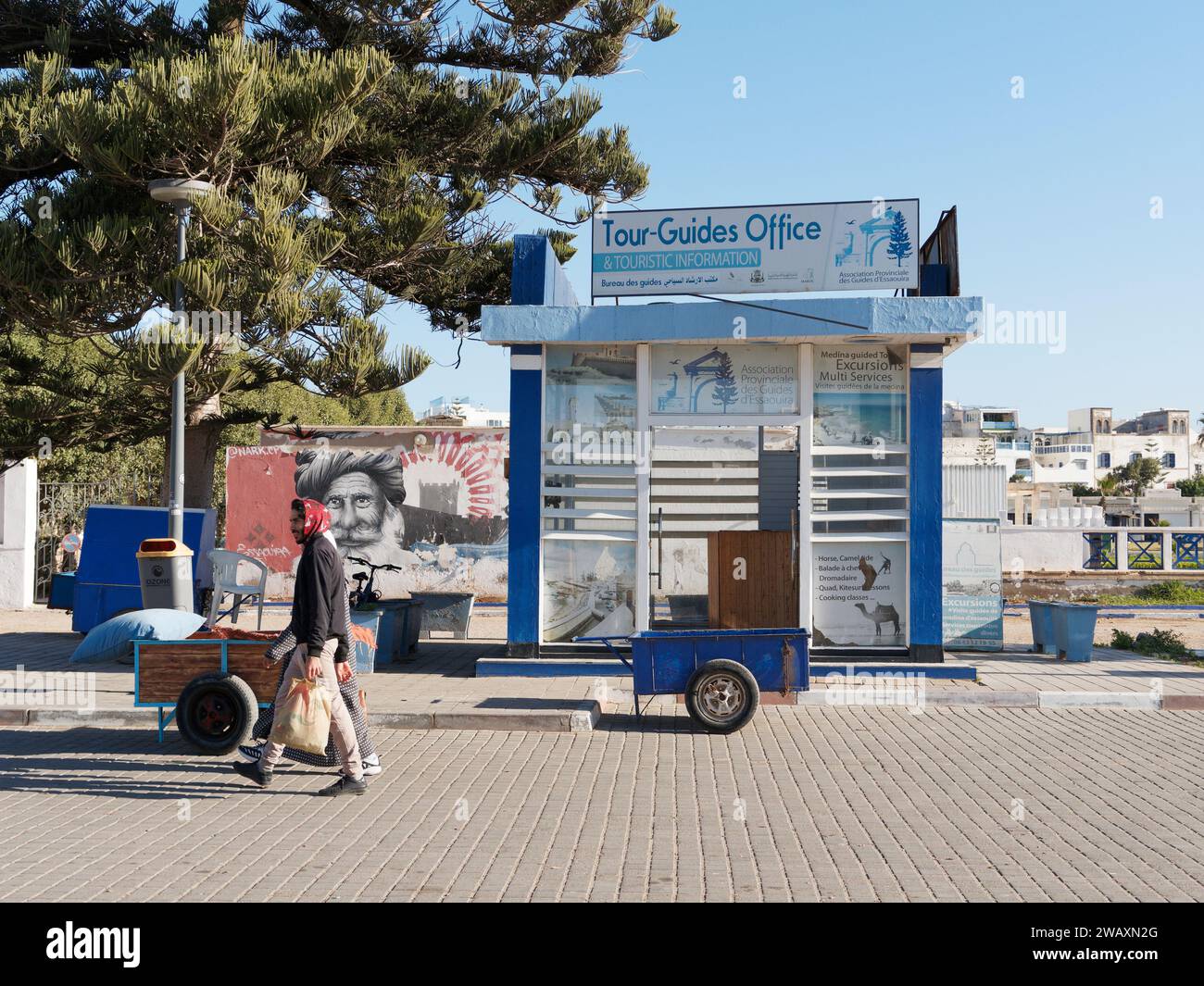 Büro für Reiseleiter/Touristeninformation mit einem Wagen draußen, während ein Mann in der Stadt Essaouira, Marokko, vorbeiläuft. Januar 2024 Stockfoto