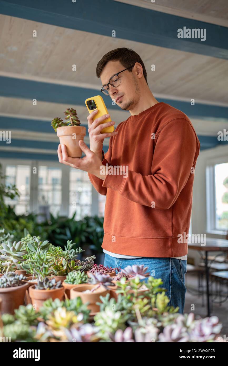 Junger Mann, der die Pflanze im Geschäft wählt, indem er Fotos macht und Informationen in mobilen Anwendungen liest Stockfoto