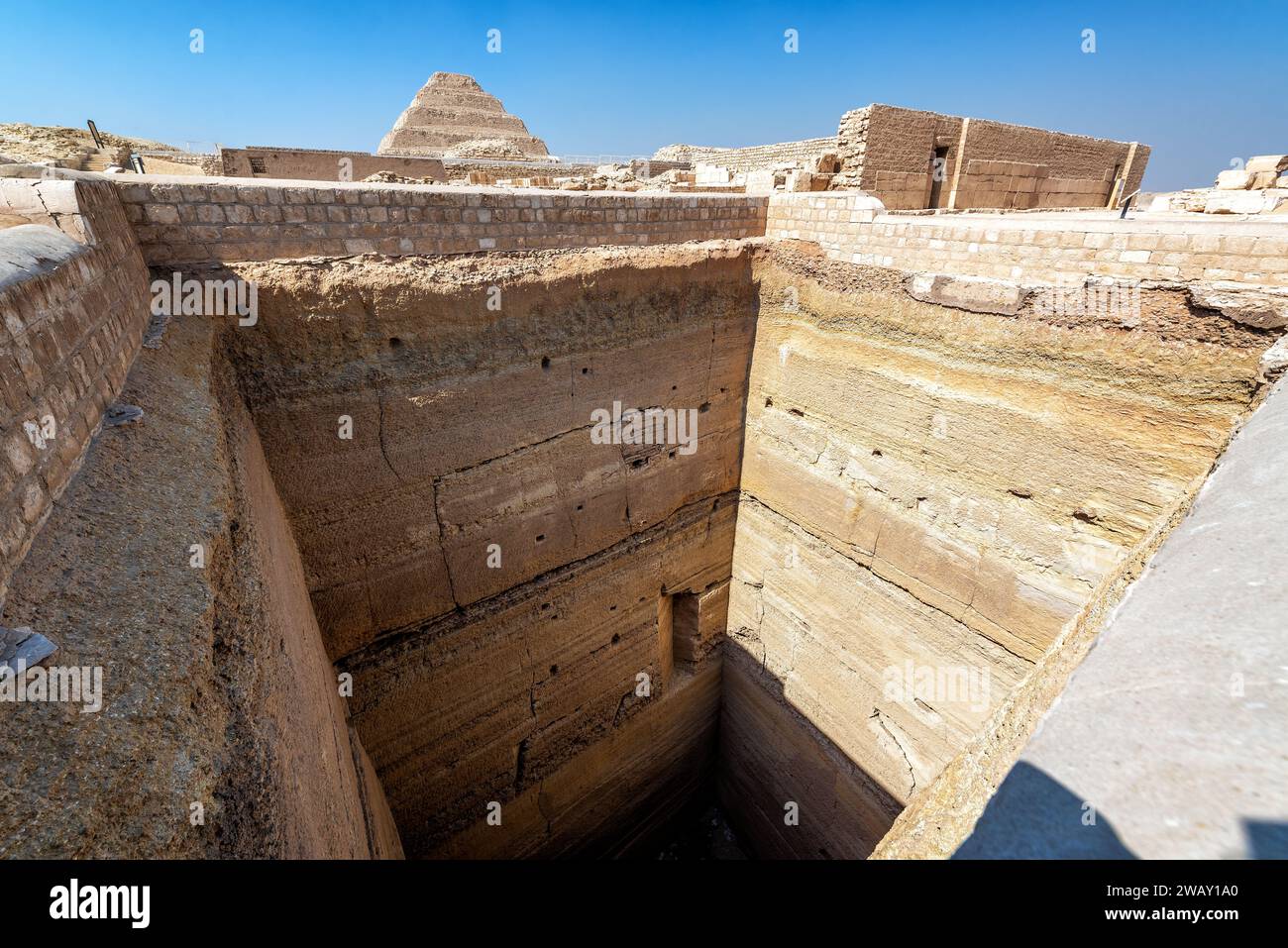 Blick auf einen langen vertikalen Schacht in Sakkara, Ägypten mit der Djoser-Pyramide im Hintergrund Stockfoto