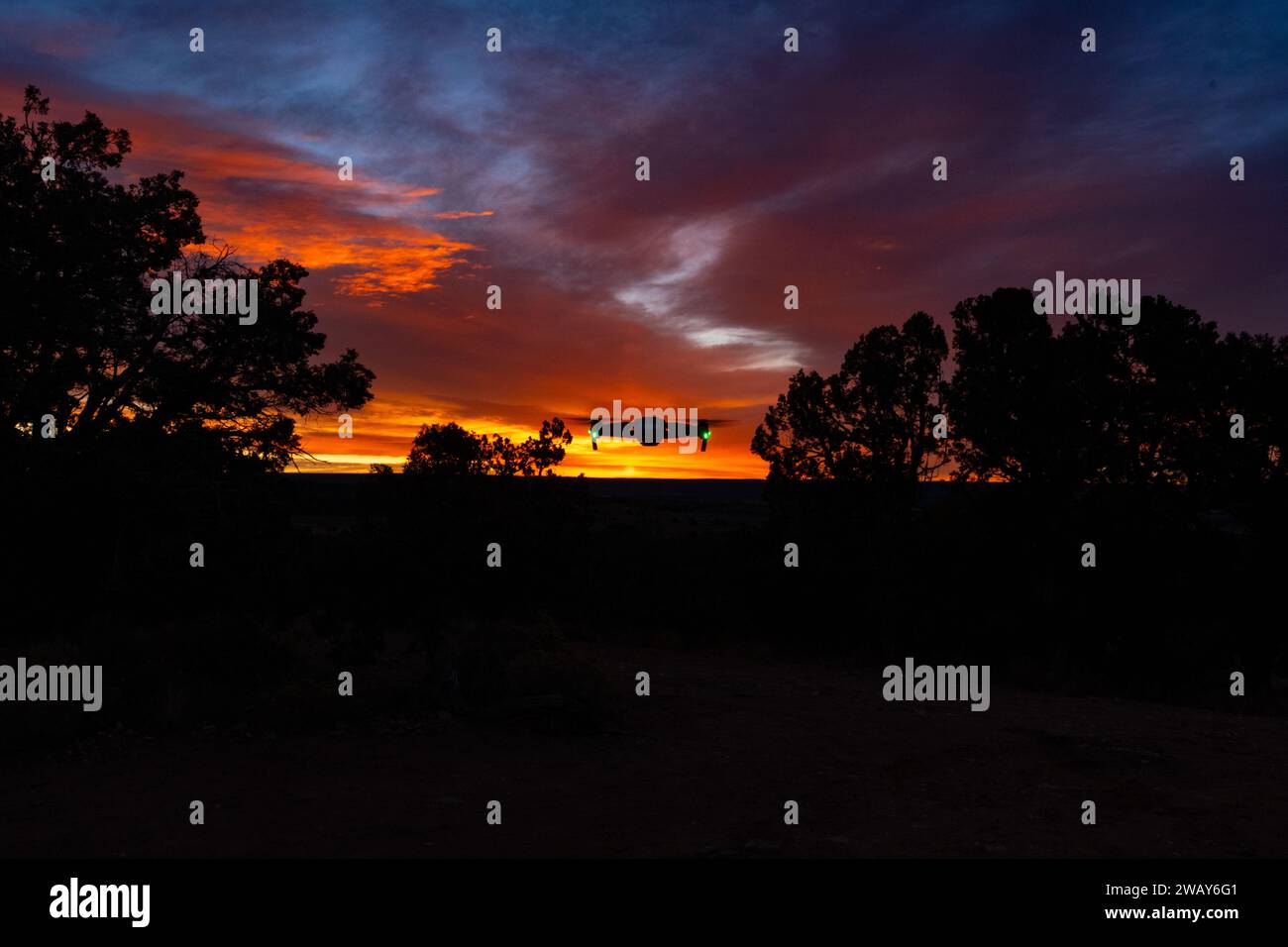 Ein atemberaubendes Bild eines Sonnenuntergangs vor dunkler Himmelskulisse mit schimmernden Wolken und Silhouetten im Vordergrund Stockfoto