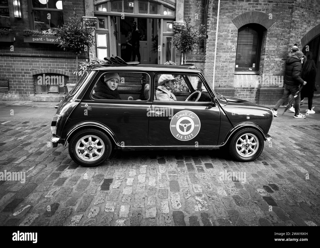 Eine Frau sitzt auf dem Rücksitz eines britischen Miniwagens auf einer Tour durch Londons kleinere Straßen in England Großbritannien Stockfoto