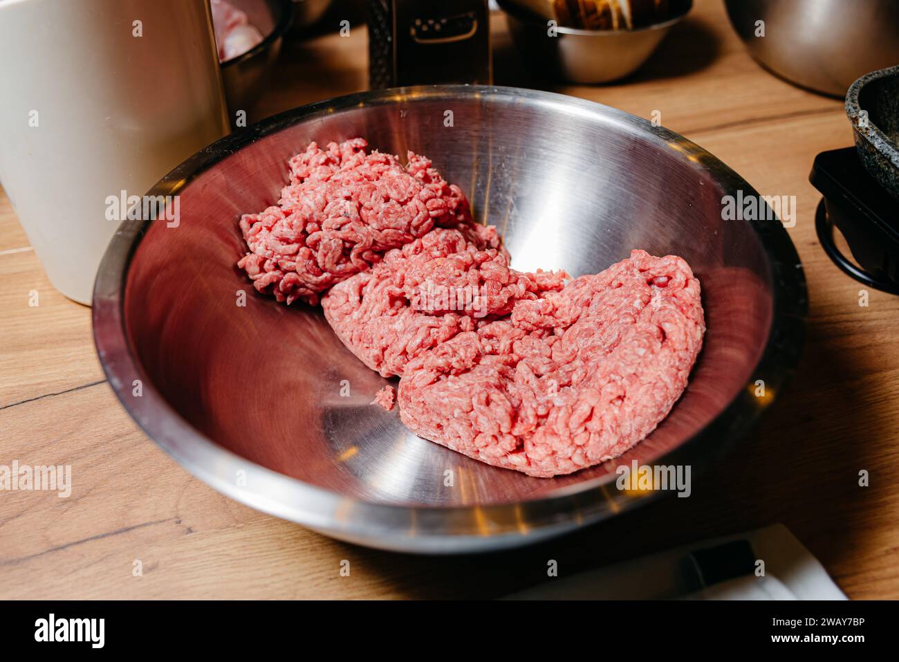 Roh gemahlenes Rindfleisch, bereit zum Kochen, in einer glänzenden Metallschale auf einer Küchenarbeitsplatte, umgeben von Kochutensilien und -Ausrüstung. Stockfoto