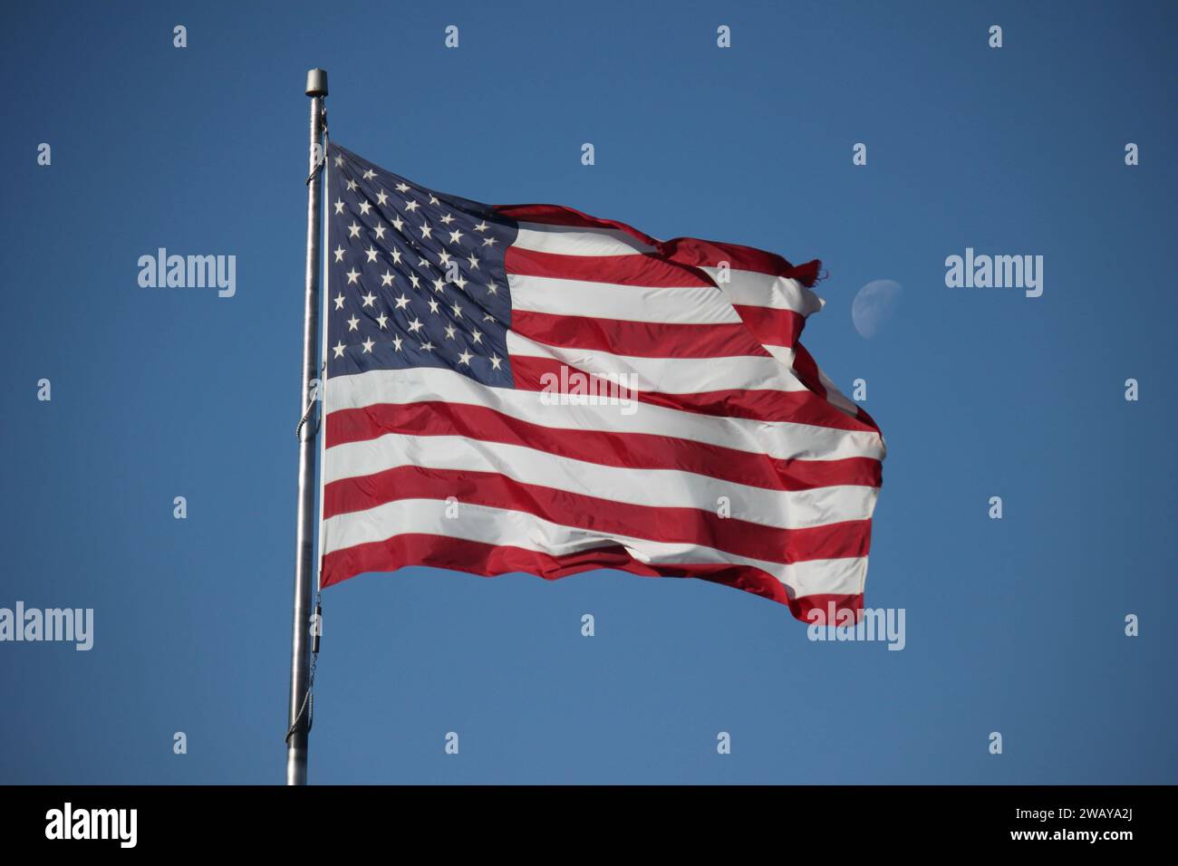 Die amerikanische Flagge weht tagsüber im Wind, während der Mond dahinter im Fokus steht Stockfoto